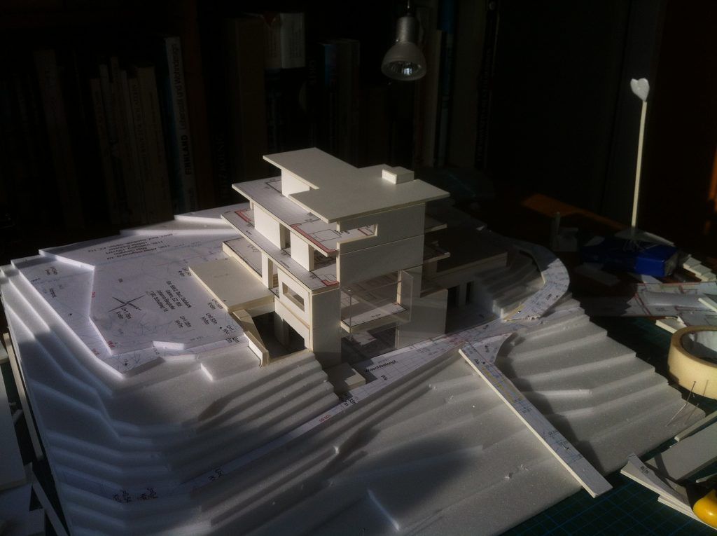 Foto eines physischen Architekturmodells aus weißer Pappe, das ein mehrgeschossiges, modernes Wohnhaus in einer gestuften Hanglage darstellt.