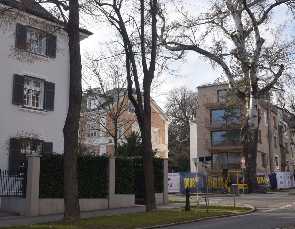 Straßenansicht in einem Wohnviertel mit klassischen Stadthäusern und einem modernen Mehrfamilienhaus mit Klinkerfassade hinter kahlen Bäumen.