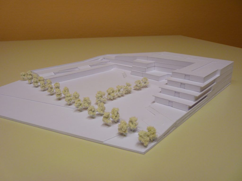 Physisches, weißes Architekturmodell eines modernen Gebäudekomplexes mit terrassenförmig abgestuften Etagen und Miniaturbäumen auf einer Freifläche.