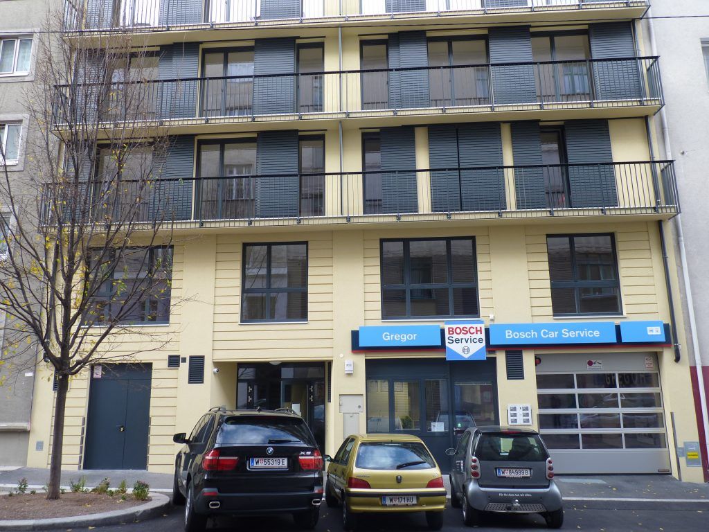 Gelbe Fassade eines Wohn- und Geschäftshauses mit einer Bosch Car Service Werkstatt im Erdgeschoss und parkenden Autos davor.